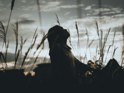 Giovane ragazza in un campo con il viso rivolto verso il cielo nuvoloso.
