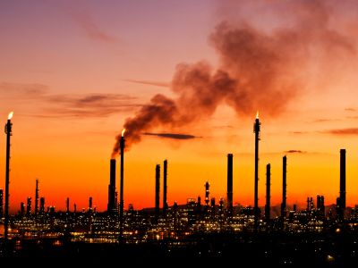 Panorama di una città al tramonto con delle fabbriche sullo sfondo che emettono gas