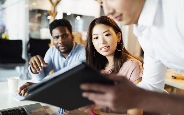 3 employees working. One employee is showing to the other 2 content on a tablet 