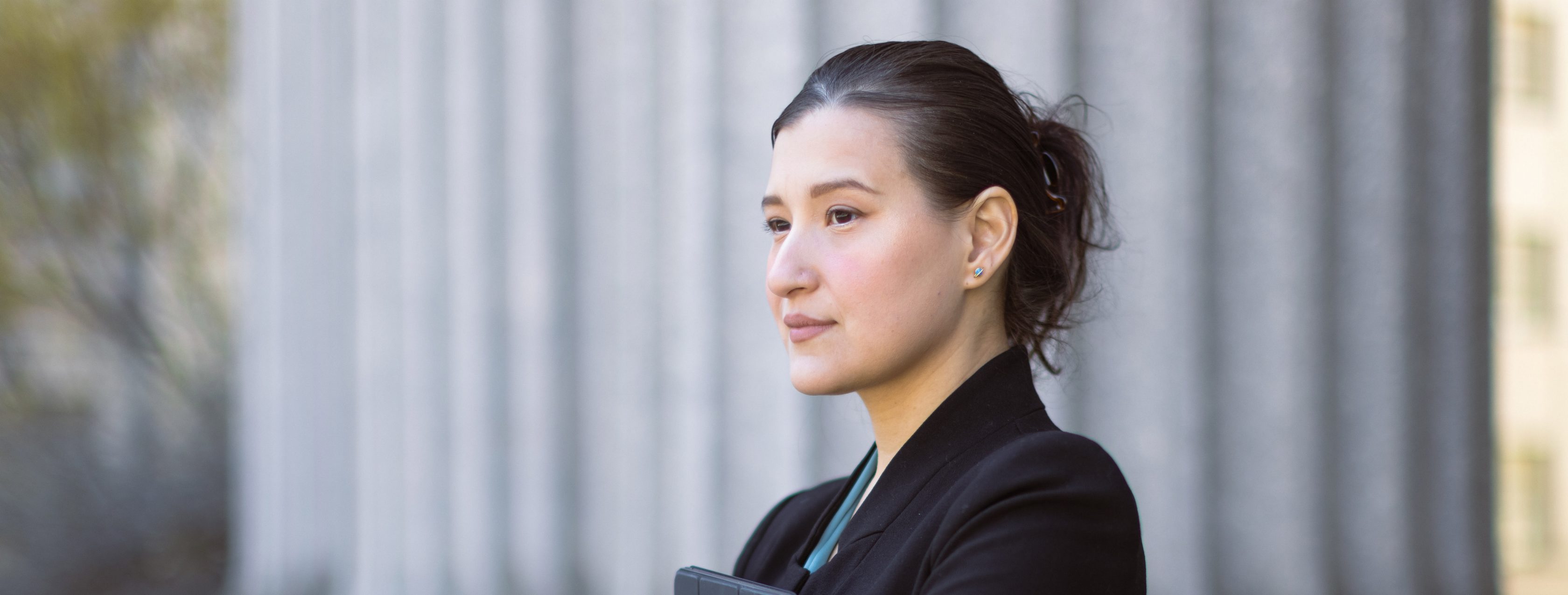 woman standing stoicly with arms crossed and folder between them