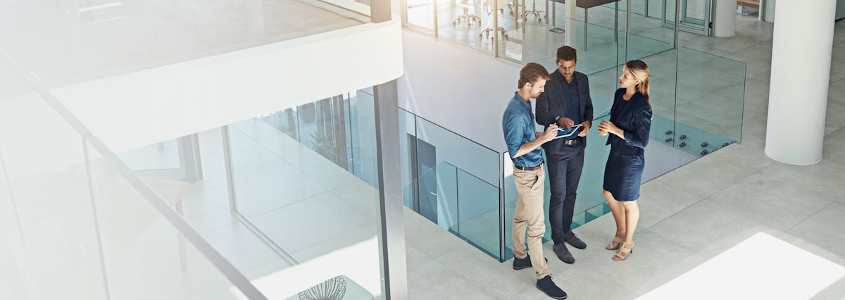 3 business people standing up and talking in a glass office