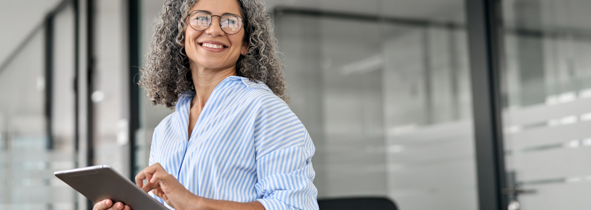 mature business woman smiling in office with tablet in hands