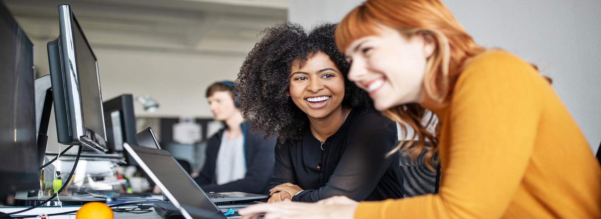 Due colleghe lavorano ad una presentazione usando i computer aziendali in ufficio