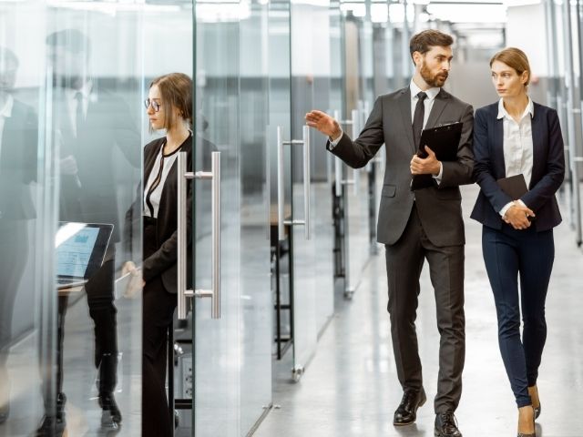 Due colleghi camminano nel corridoio con pareti di vetro dell'ufficio