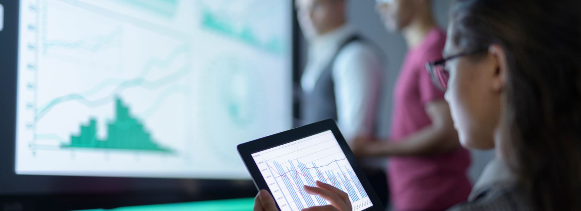 Tre data analyst controllano l'andamento di un grafico su un tablet e su un grande schermo