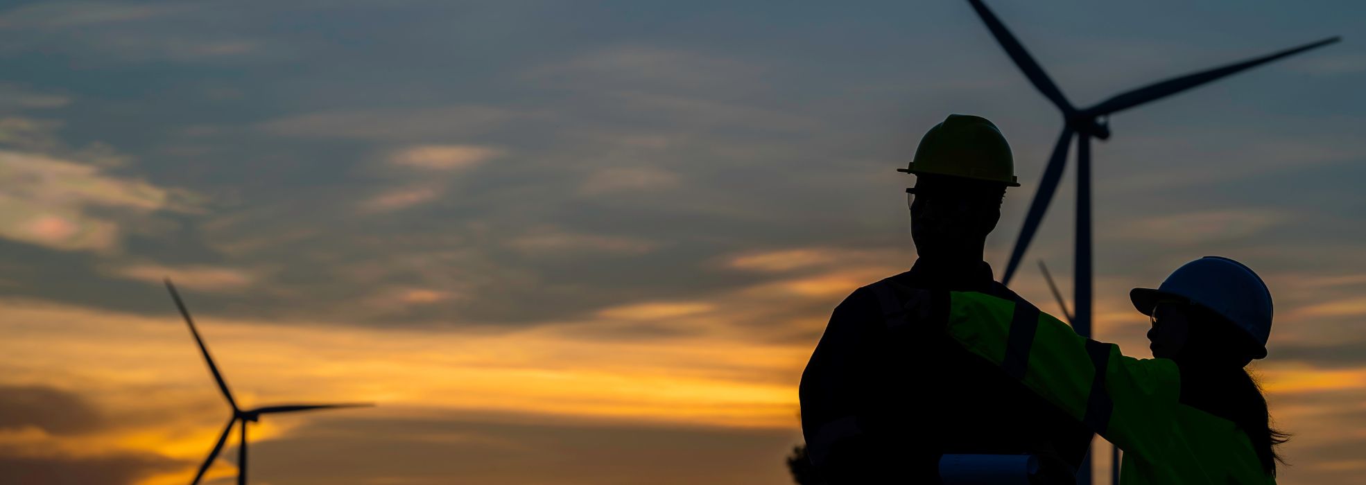 Due tecnici di impianti eolici si occupano della manutenzione di un parco eolico al tramonto
