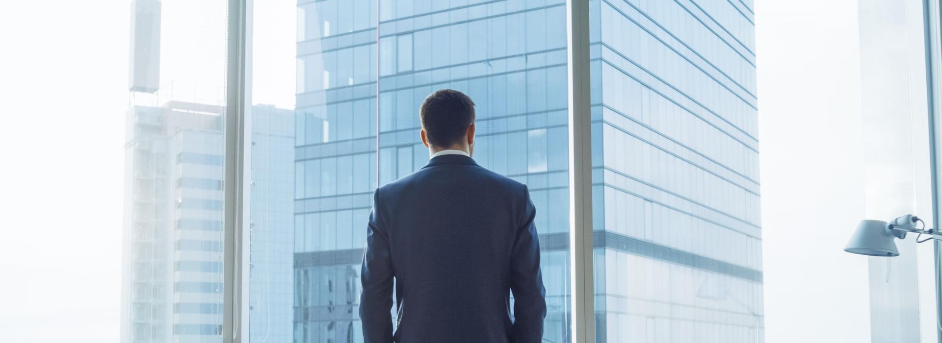 Un manager di spalle osserva la vista della città dalla vetrata del suo ufficio