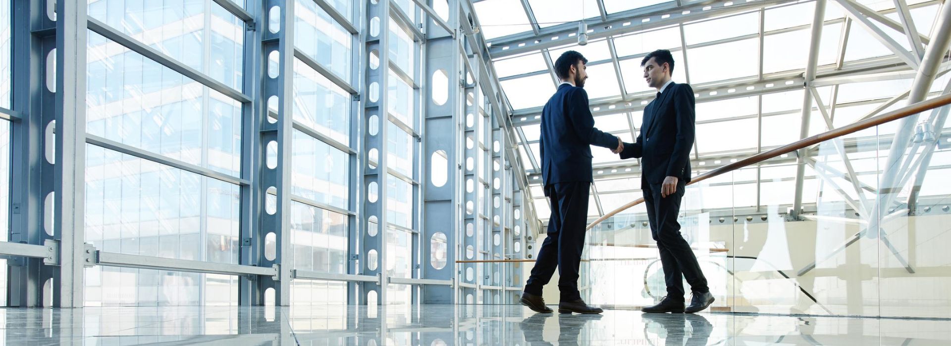 Due imprenditori si stirngolo la mano in un edificio luminoso e con vetrate