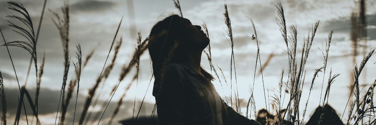 Giovane ragazza in un campo con il viso rivolto verso il cielo nuvoloso.