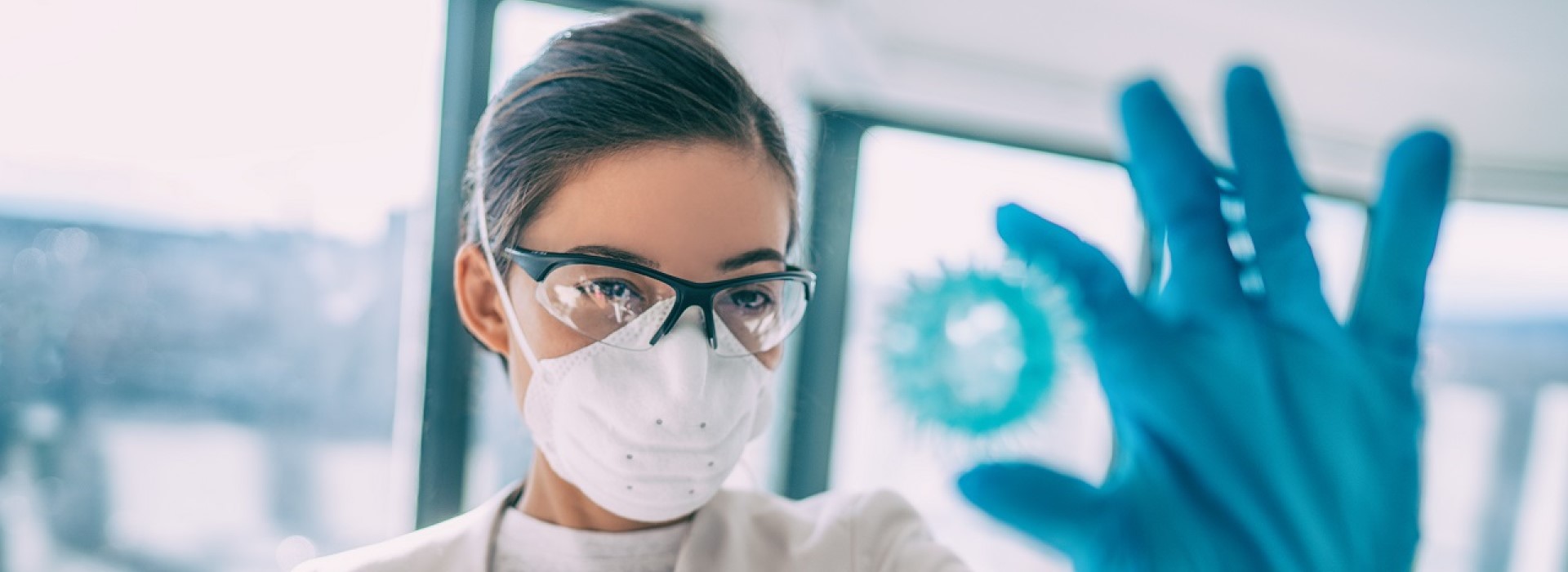 Primo piano di ricercatrice che indossa guanti, mascherina e occhiali protettivi