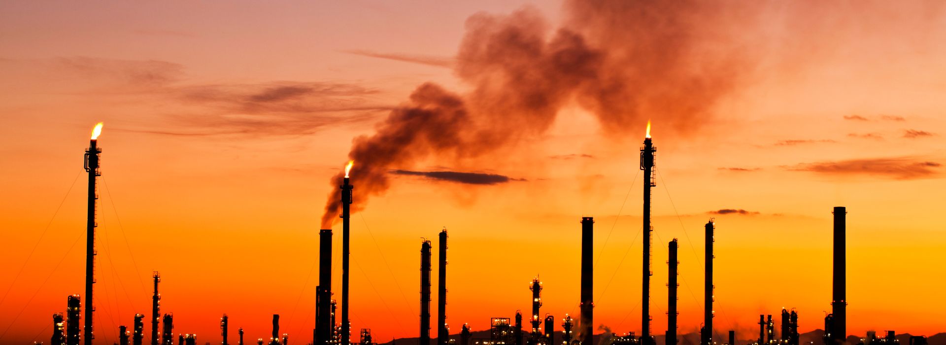 Panorama di una città al tramonto con delle fabbriche sullo sfondo che emettono gas