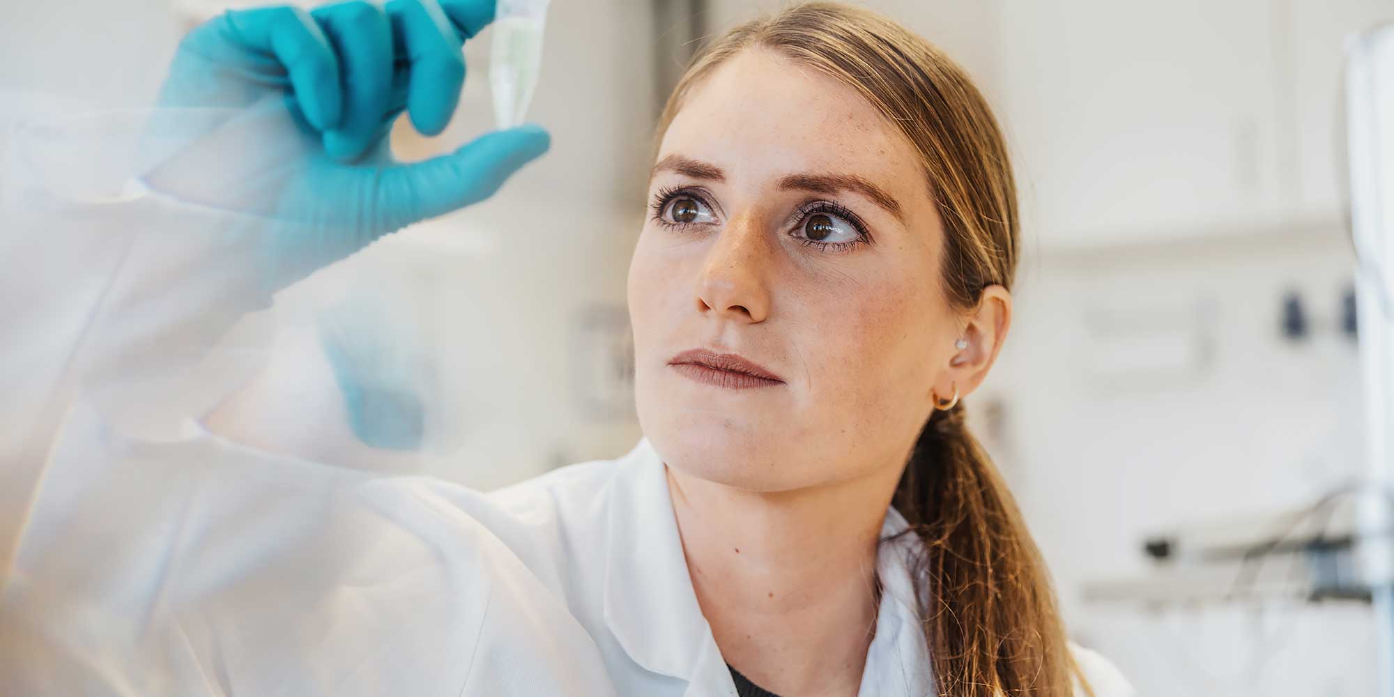 Kobieta w niebieskiej rękawiczce patrzy na trzymaną fiolkę