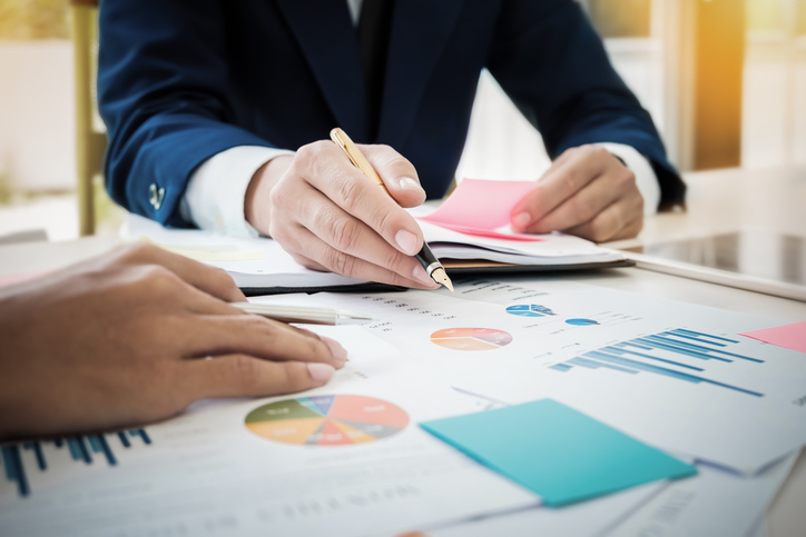 Illustration: Arbeitsplatz an dem zwei anwesenden Personen Diagramme und Auswertungen besprechen