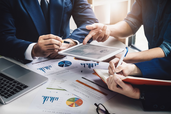Illustration: Arbeitsplatz an dem mehrere anwesende Personen Diagramme und Auswertungen besprechen