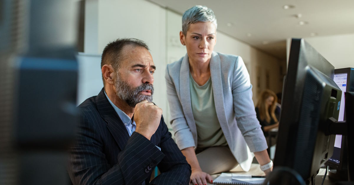 homme et femme à l'air sérieux devant un écran d'ordinateur
