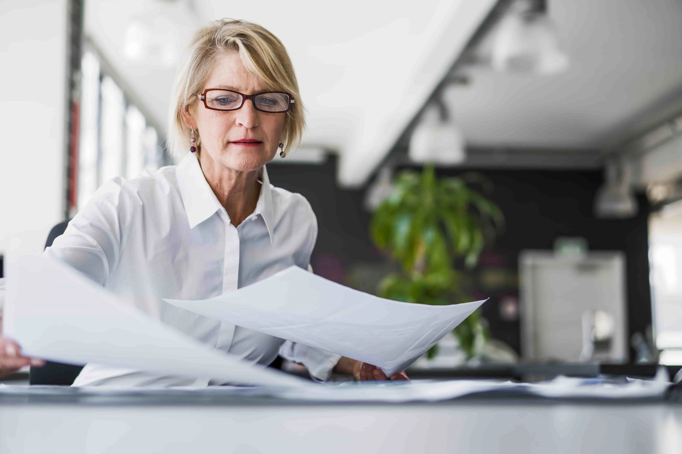 Une femme blonde avec des lunettes lit des documents