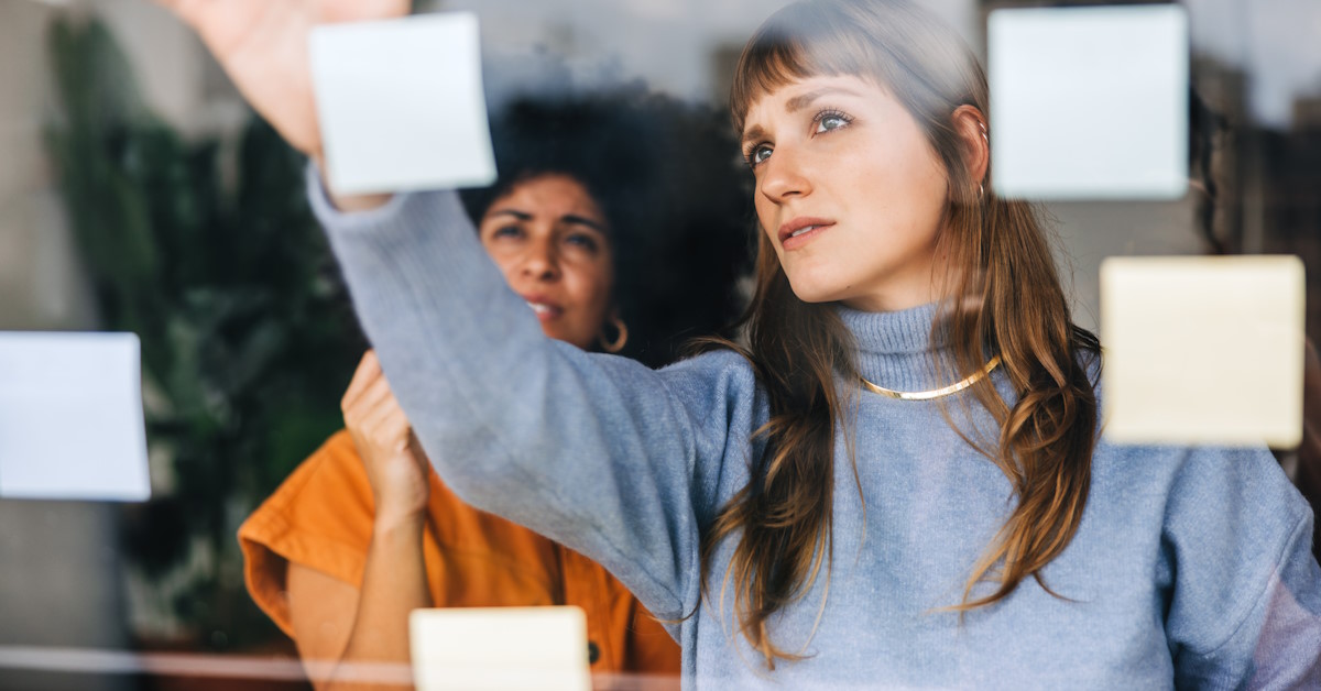 Deux personnes font face à un tableau et collent des post-its